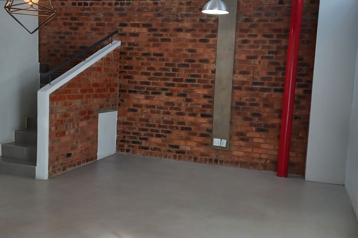 Spacious open-plan living area featuring industrial-style exposed brick walls, polished concrete floors, and a staircase with a modern metal handrail.
