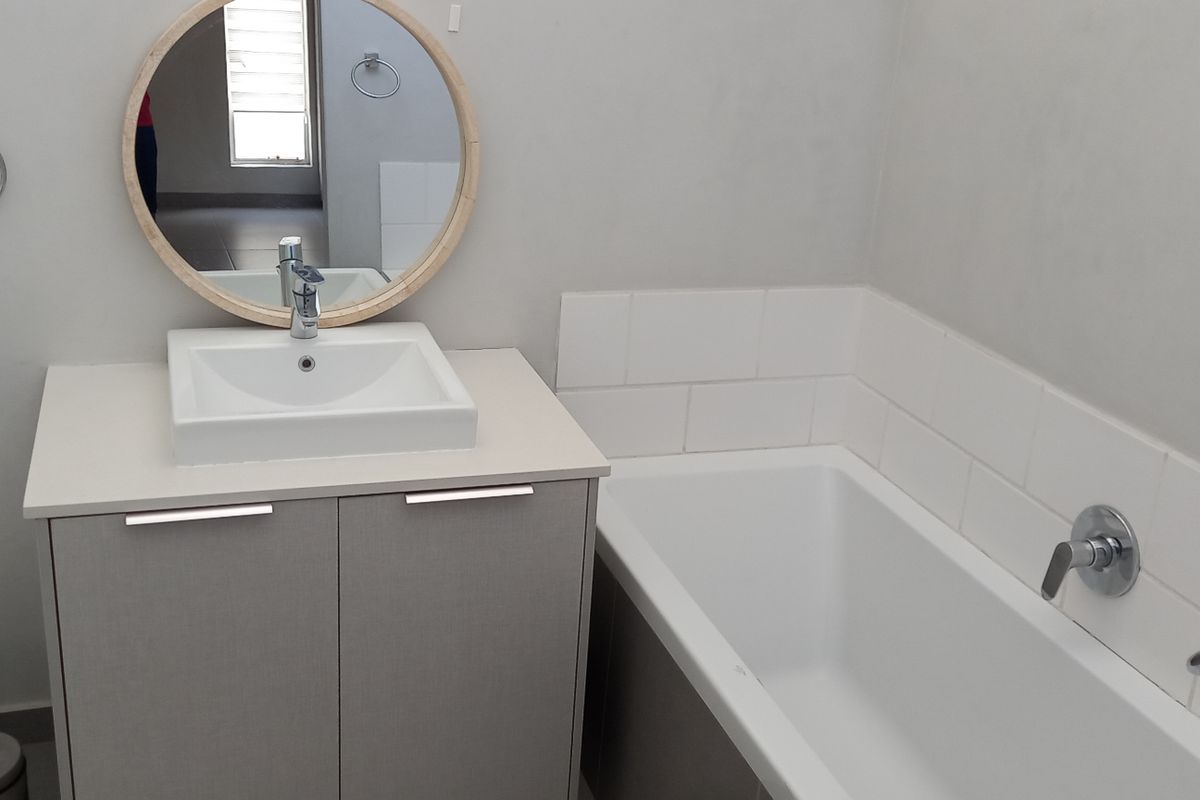 A modern bathroom featuring a vanity with a countertop basin, a bathtub with wall-mounted fixtures, and neutral wall finishes.
