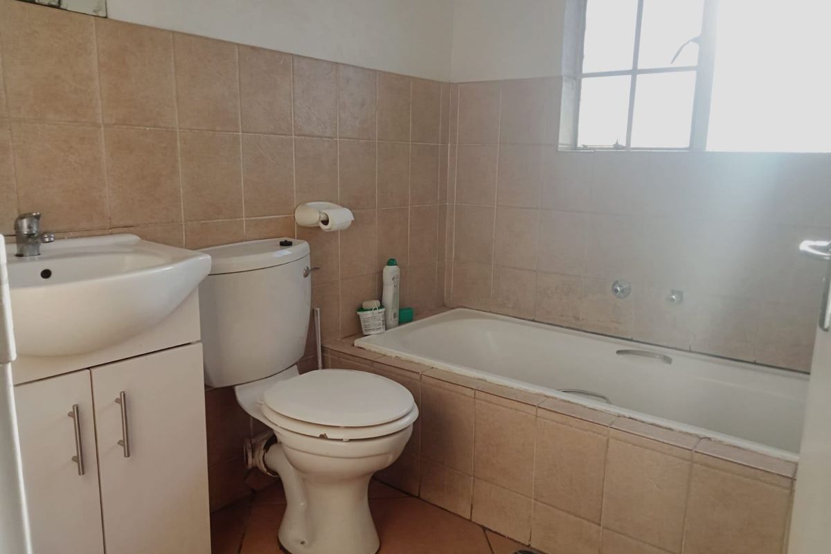 A functional bathroom featuring a built-in bathtub, vanity cabinet with basin, and toilet, finished with neutral ceramic wall and floor tiles.