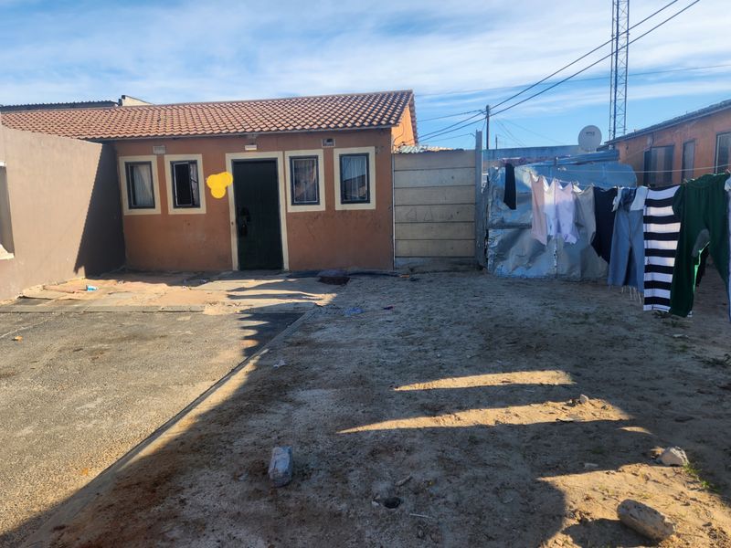Rear exterior view of the property featuring a tiled roof, concrete paving, and a sandy yard area with boundary walling.