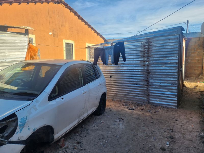 Rear yard area featuring a corrugated metal storage structure and masonry boundary walling on an unpaved surface.