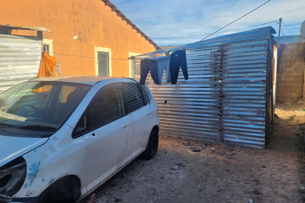 Rear yard area featuring a corrugated metal storage structure and masonry boundary walling on an unpaved surface.