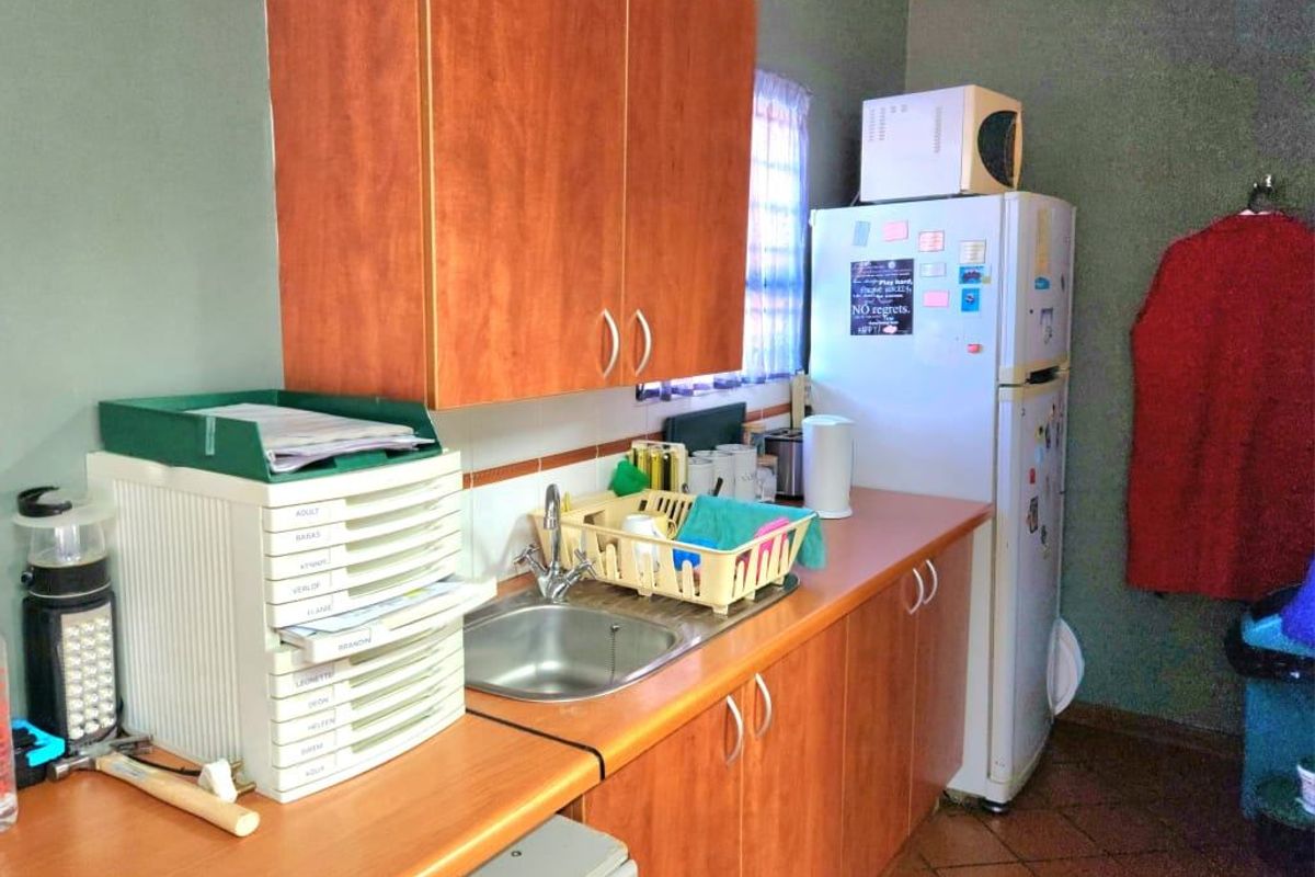 A functional kitchen area featuring wood-look laminate cabinetry, a stainless steel sink, tiled backsplash, and durable tiled flooring.