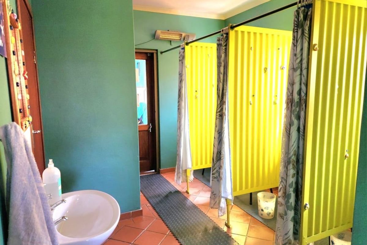 Commercial bathroom facility featuring a pedestal washbasin and multiple shower stalls with corrugated metal partitions and curtains.