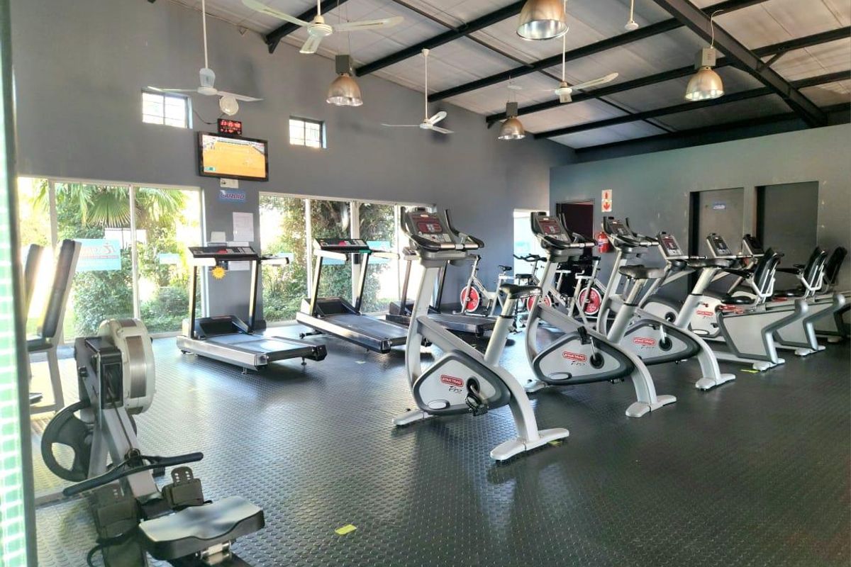A well-maintained commercial gym facility featuring durable rubberized flooring, exposed industrial roof trusses, and ample natural light through large windows.