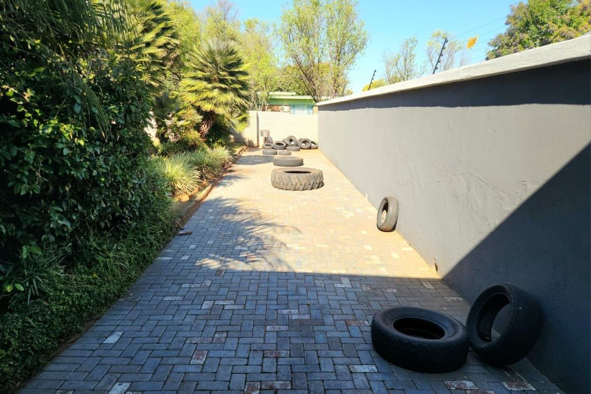 A paved side or rear exterior area featuring a high boundary wall with electric fencing and established garden greenery.
