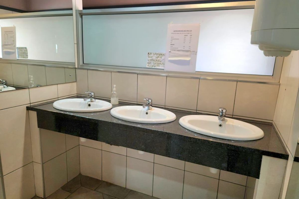 Commercial bathroom vanity area featuring a triple sink setup with granite countertops, tiled splashbacks, and a large wall-mounted mirror.