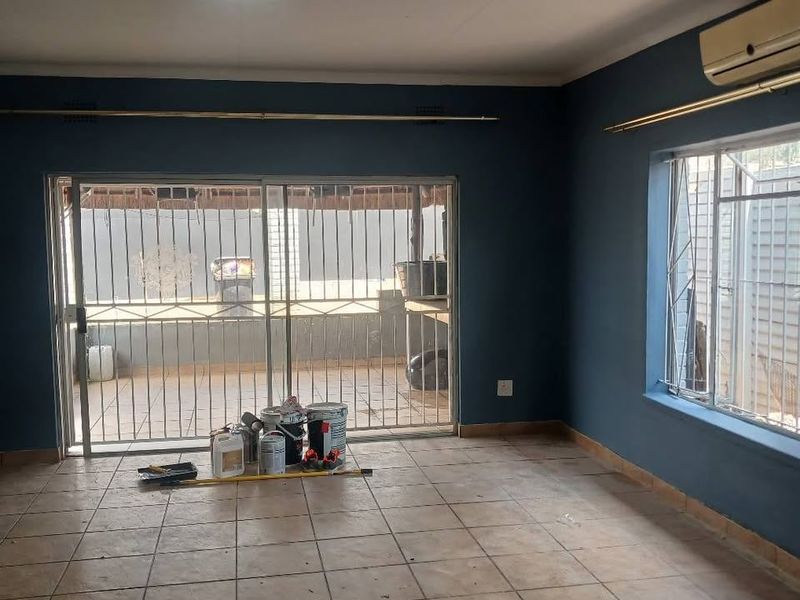 An empty living room featuring tiled flooring, an air conditioning unit, and large sliding glass doors with security bars leading to an outdoor area.