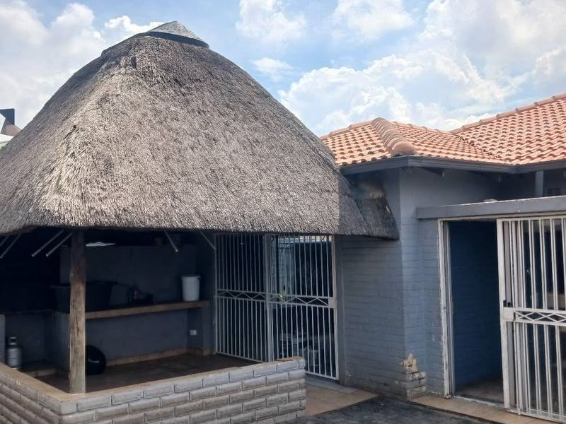 Covered outdoor patio area featuring a traditional thatch roof, built-in braai, and secure gated access to the main house.