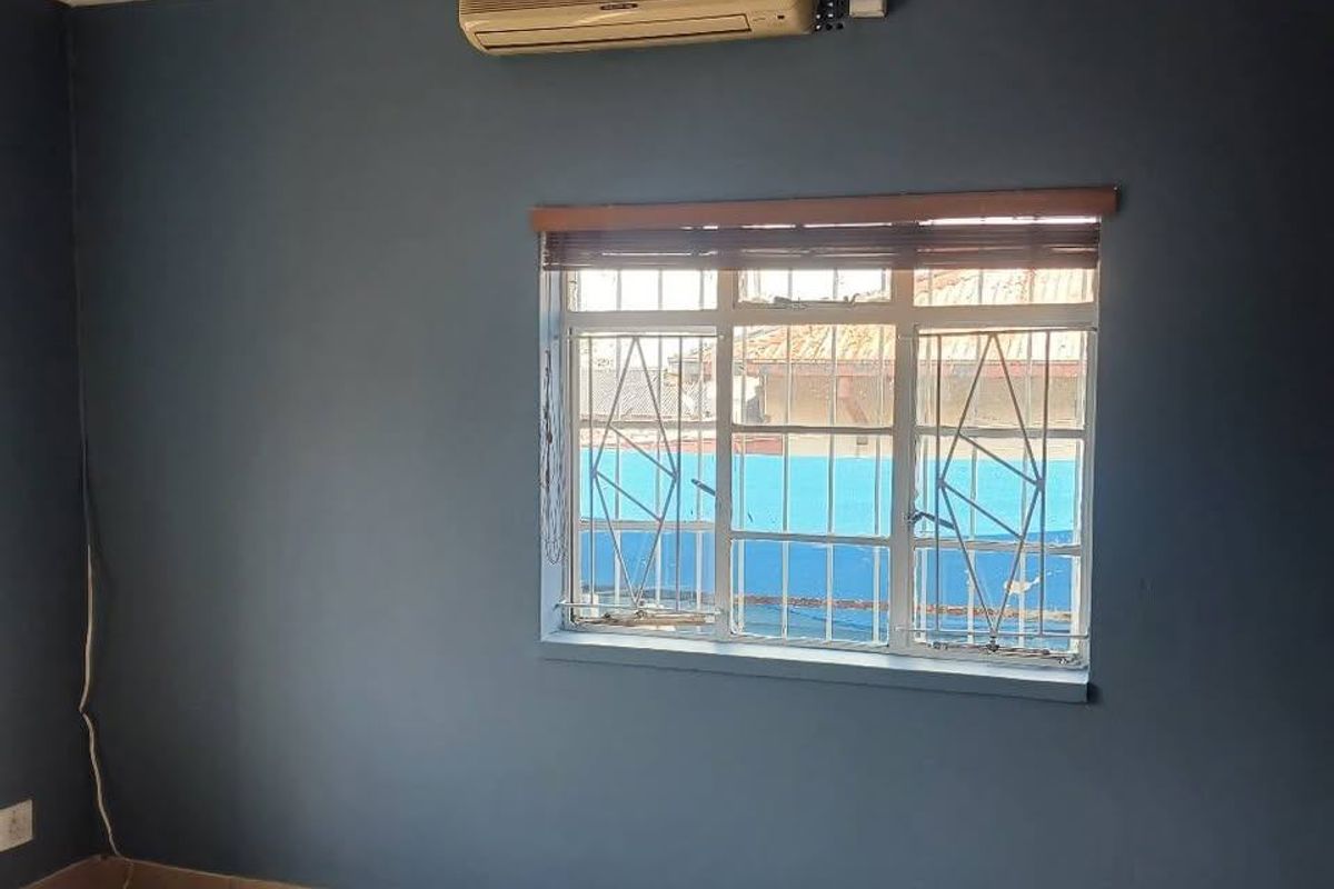 An empty bedroom featuring tiled flooring, a wall-mounted air conditioning unit, and a window fitted with security bars.