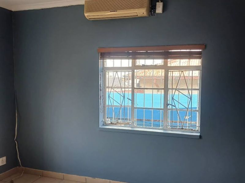 An empty bedroom featuring tiled flooring, a wall-mounted air conditioning unit, and a window fitted with security bars.