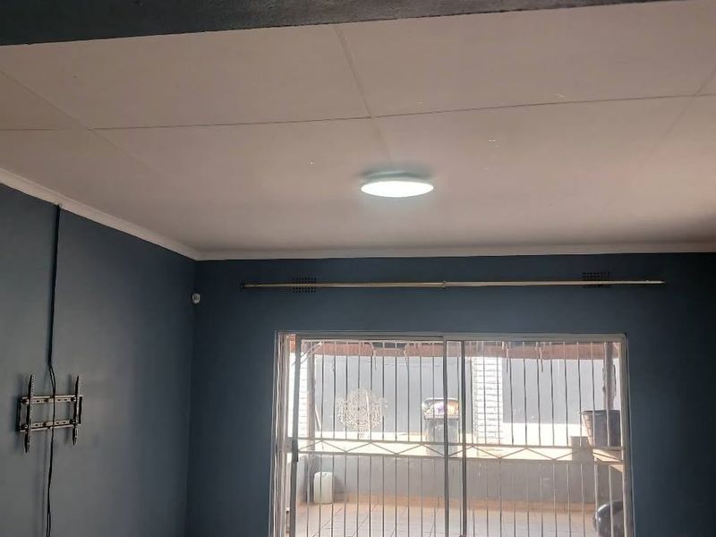 An empty living room featuring dark blue walls, tiled flooring, and a sliding glass door with security gate leading to an outdoor area.