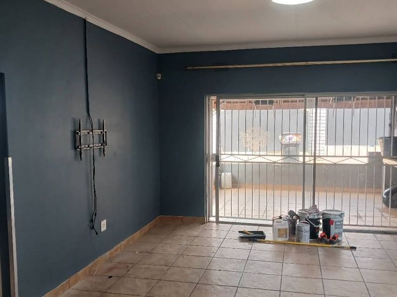 An empty living room featuring dark blue accent walls, ceramic tile flooring, and a sliding glass door with security bars leading to the patio.