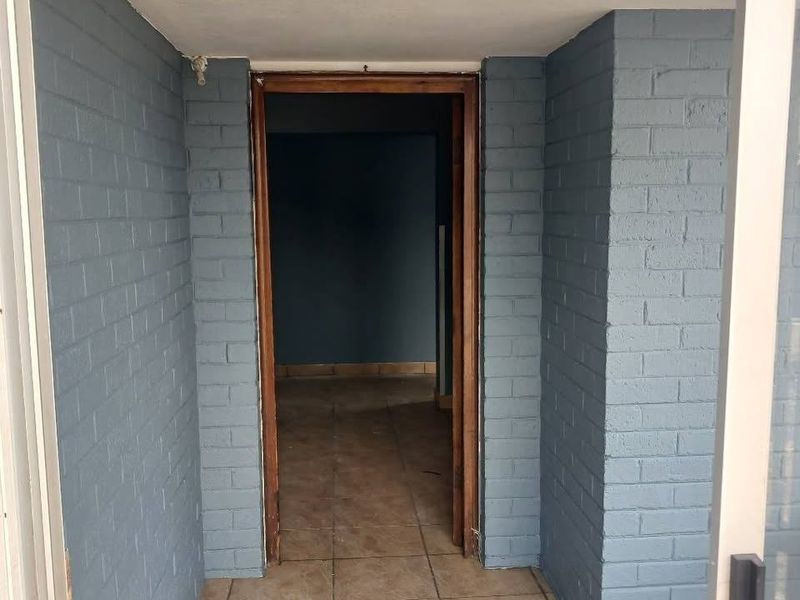 An empty entrance area featuring painted brick walls, tiled flooring, and a timber door frame leading into the interior of the home.