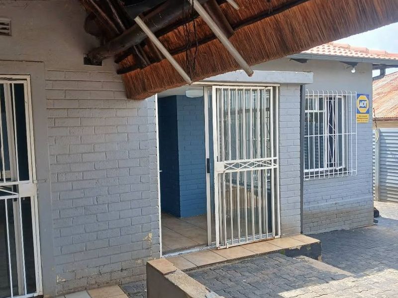 Covered patio area featuring a thatch roof, tiled flooring, and security gates, providing access to the main dwelling.