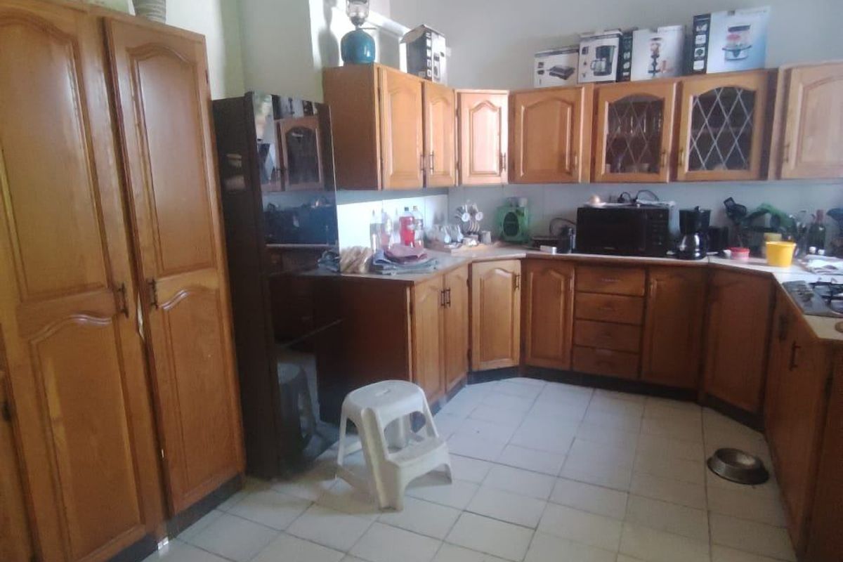 A dated kitchen featuring traditional wooden cabinetry, tiled flooring, and classic cornice detailing, offering significant potential for a modern renovation.