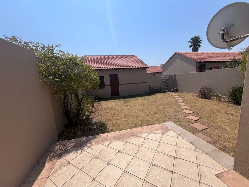 A private rear garden featuring a tiled patio, paved stepping stones, and perimeter boundary walls, providing a functional outdoor space for the townhouse.