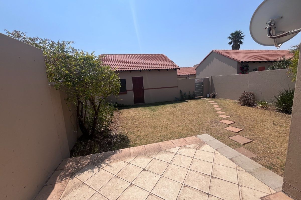 A private rear garden featuring a tiled patio, paved stepping stones, and perimeter boundary walls, providing a functional outdoor space for the townhouse.