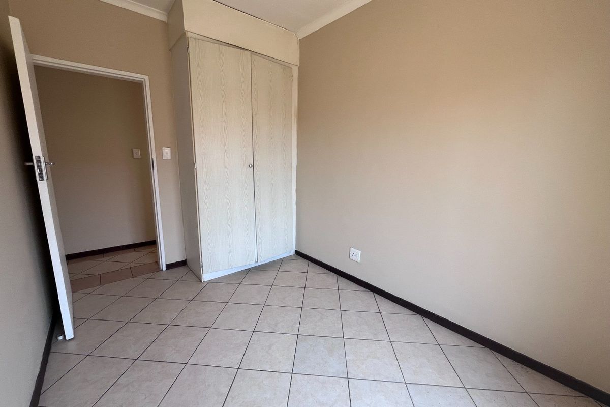 A vacant bedroom featuring neutral wall paint, tiled flooring, and a built-in cupboard, offering a clean and versatile space ready for personalization.