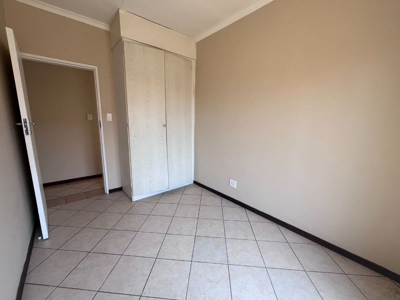 A vacant bedroom featuring neutral wall paint, tiled flooring, and a built-in cupboard, offering a clean and versatile space ready for personalization.