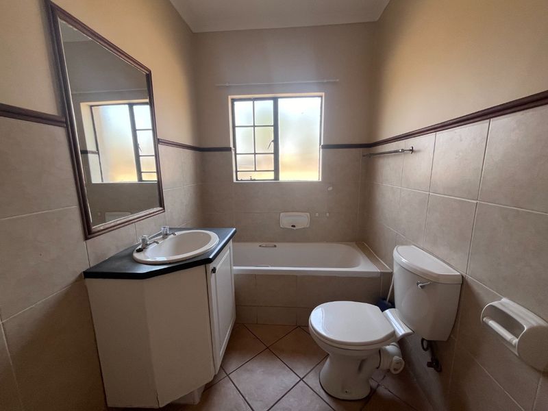 A functional bathroom featuring a built-in vanity, bathtub, and toilet with neutral wall and floor tiling.