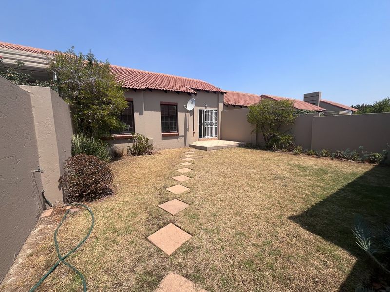 A private rear garden featuring a tiled roof townhouse facade, a paved patio area, and a stone pathway leading to the entrance.