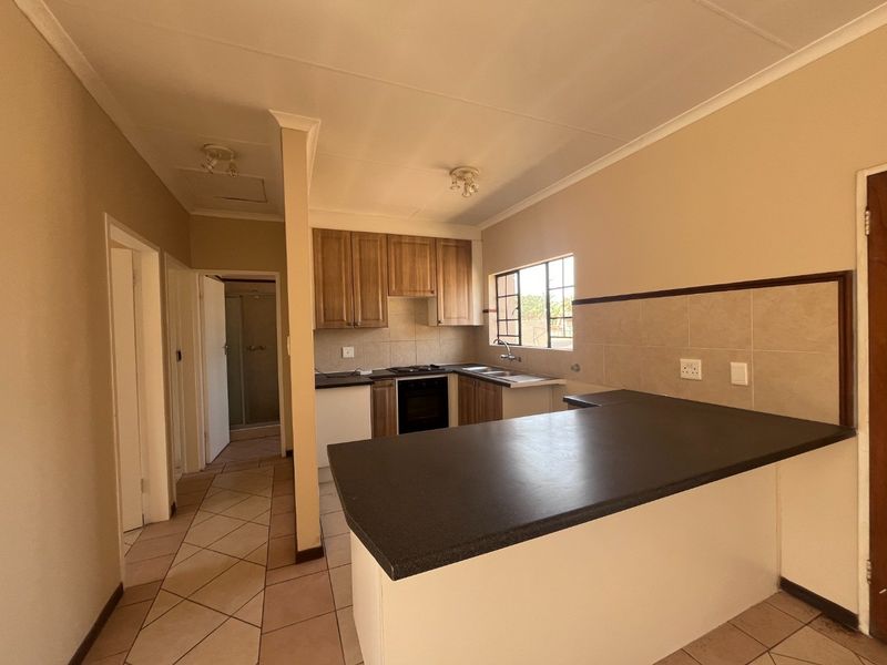 A functional kitchen featuring built-in wooden cabinetry, dark laminate countertops, a breakfast bar, and tiled flooring, offering a clean and practical layout.