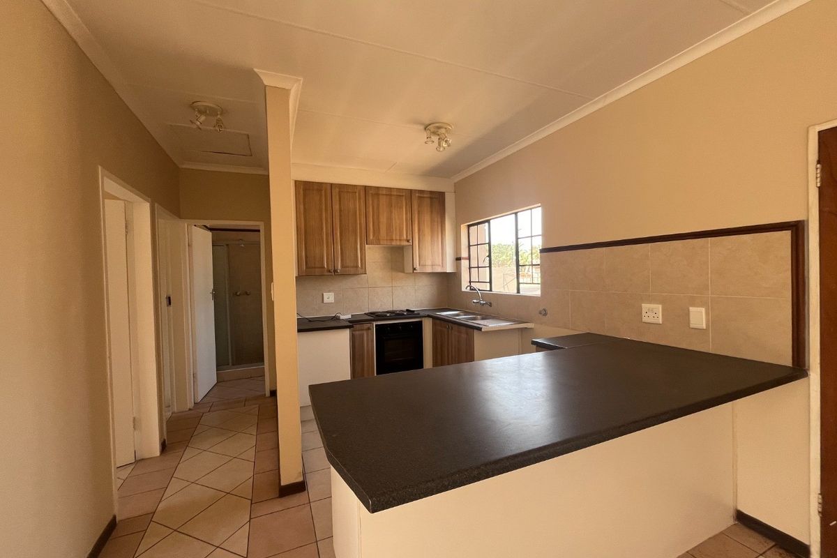 A functional kitchen featuring built-in wooden cabinetry, dark laminate countertops, a breakfast bar, and tiled flooring, offering a clean and practical layout.
