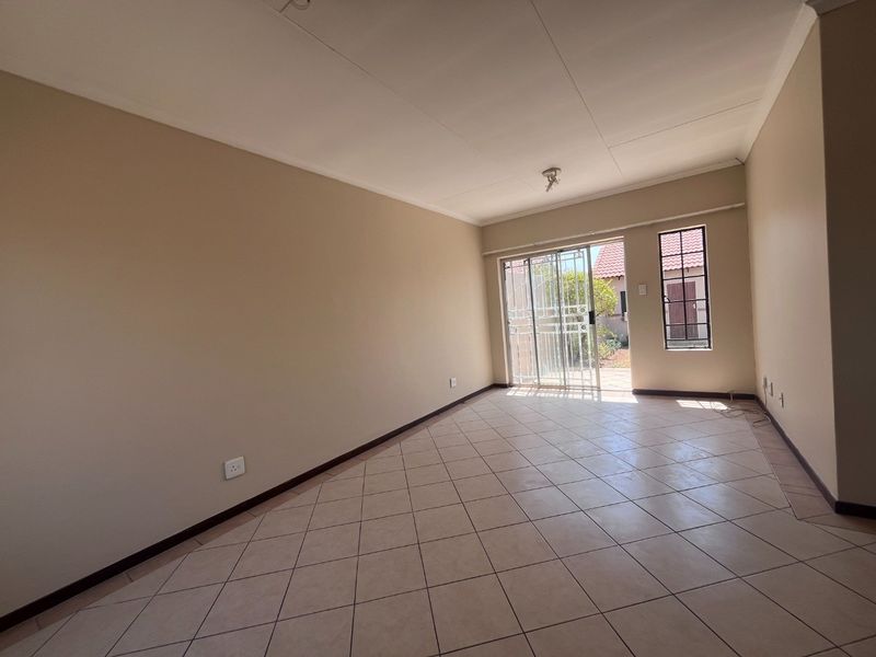 A spacious, empty living area featuring neutral wall tones, tiled flooring, and a sliding glass door providing access to the rear exterior.