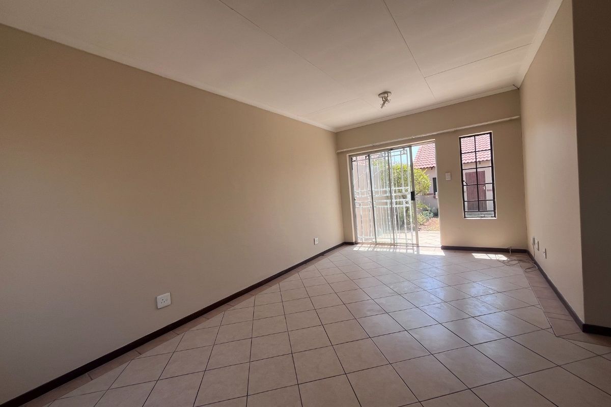 A spacious, empty living area featuring neutral wall tones, tiled flooring, and a sliding glass door providing access to the rear exterior.
