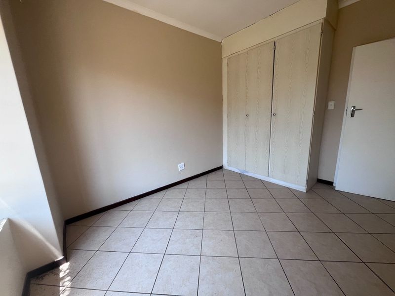 An empty bedroom featuring neutral wall paint, tiled flooring, and built-in cupboards, offering a blank canvas for personalization.
