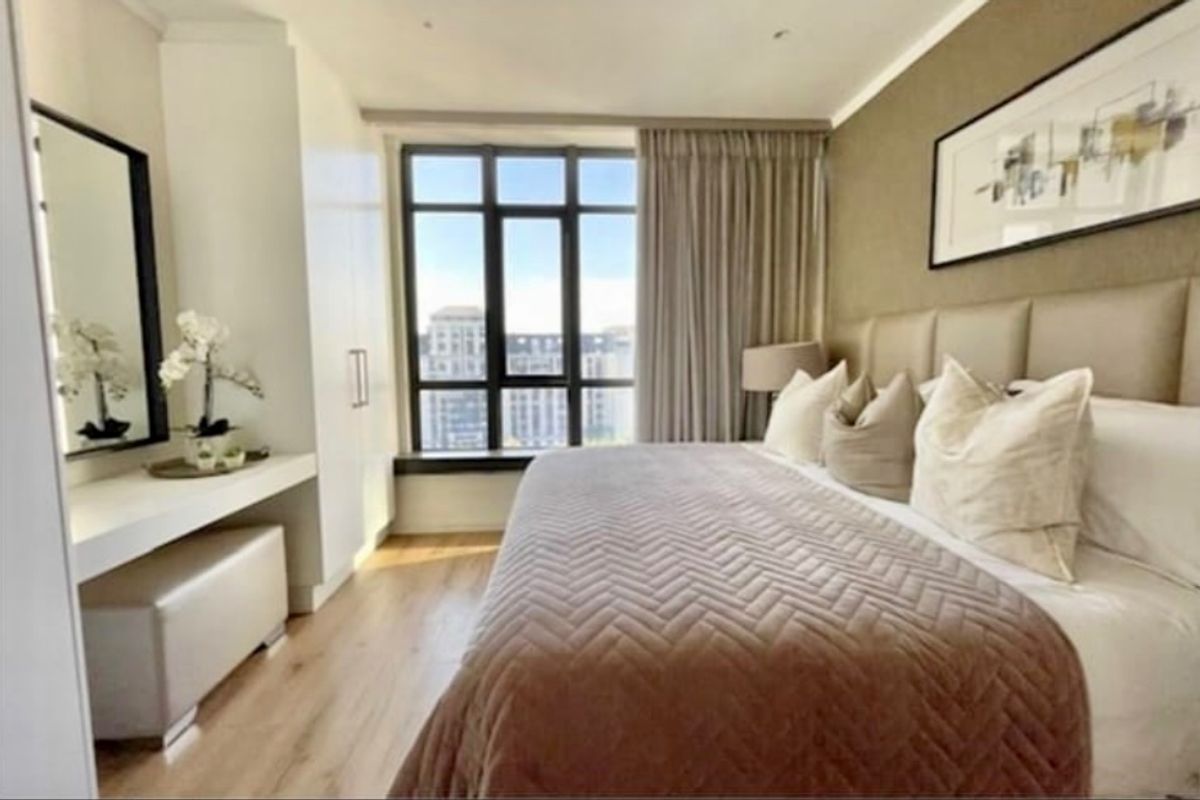 A well-appointed bedroom featuring built-in cabinetry, a vanity unit, laminate flooring, and large windows providing natural light and urban views.