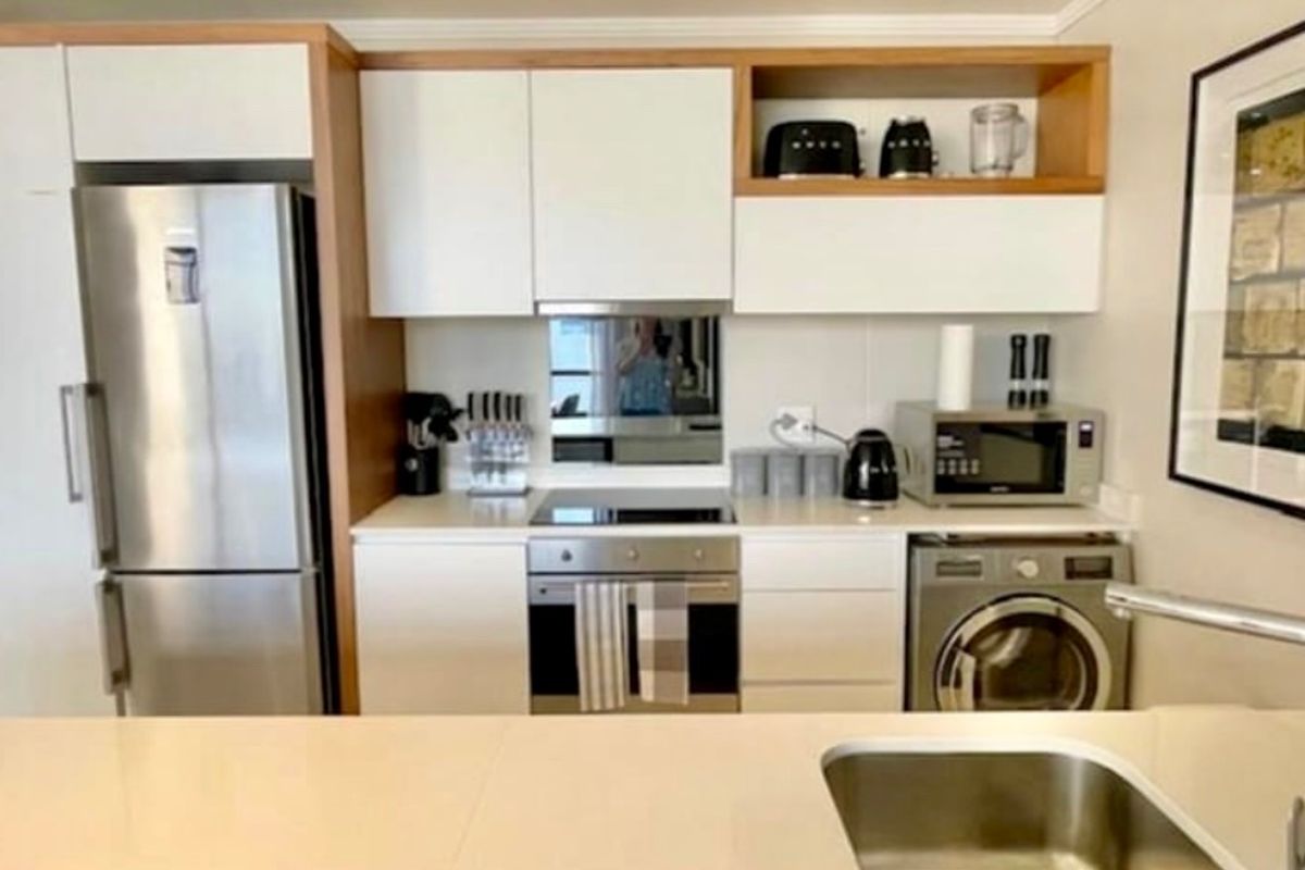 Modern compact kitchen featuring white cabinetry, stone countertops, integrated stainless steel appliances, and a mirrored splashback.