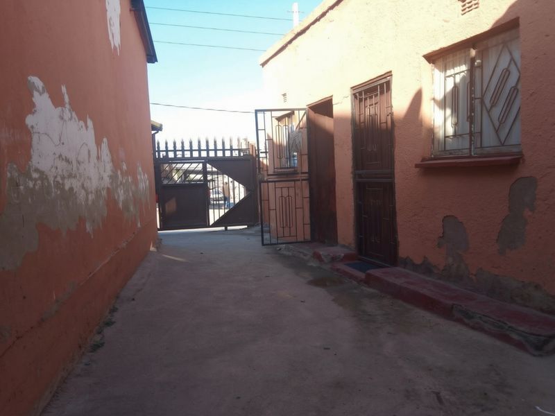 Exterior view of the property entrance featuring a concrete driveway, security gate, and security bars on windows, showing signs of exterior wall wear.