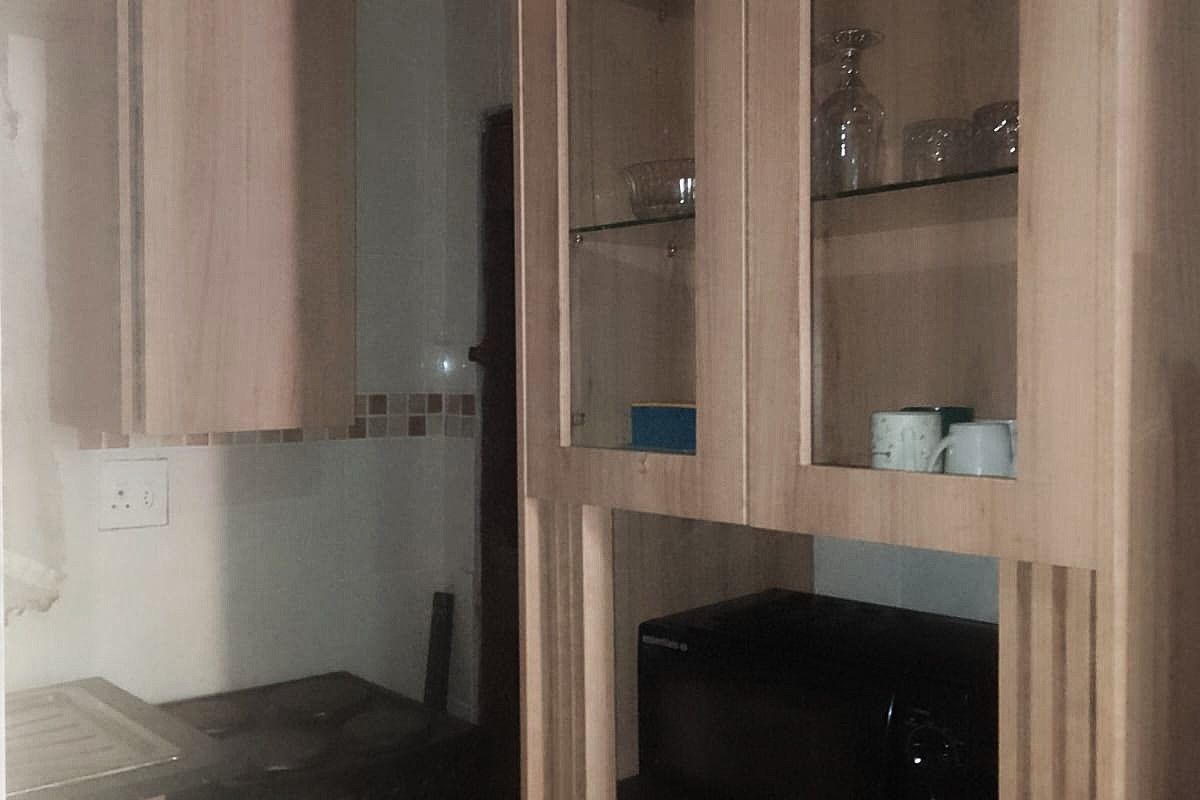 A compact kitchen featuring light wood-toned cabinetry, a tiled backsplash, and a dedicated built-in microwave shelf with integrated glass display storage.