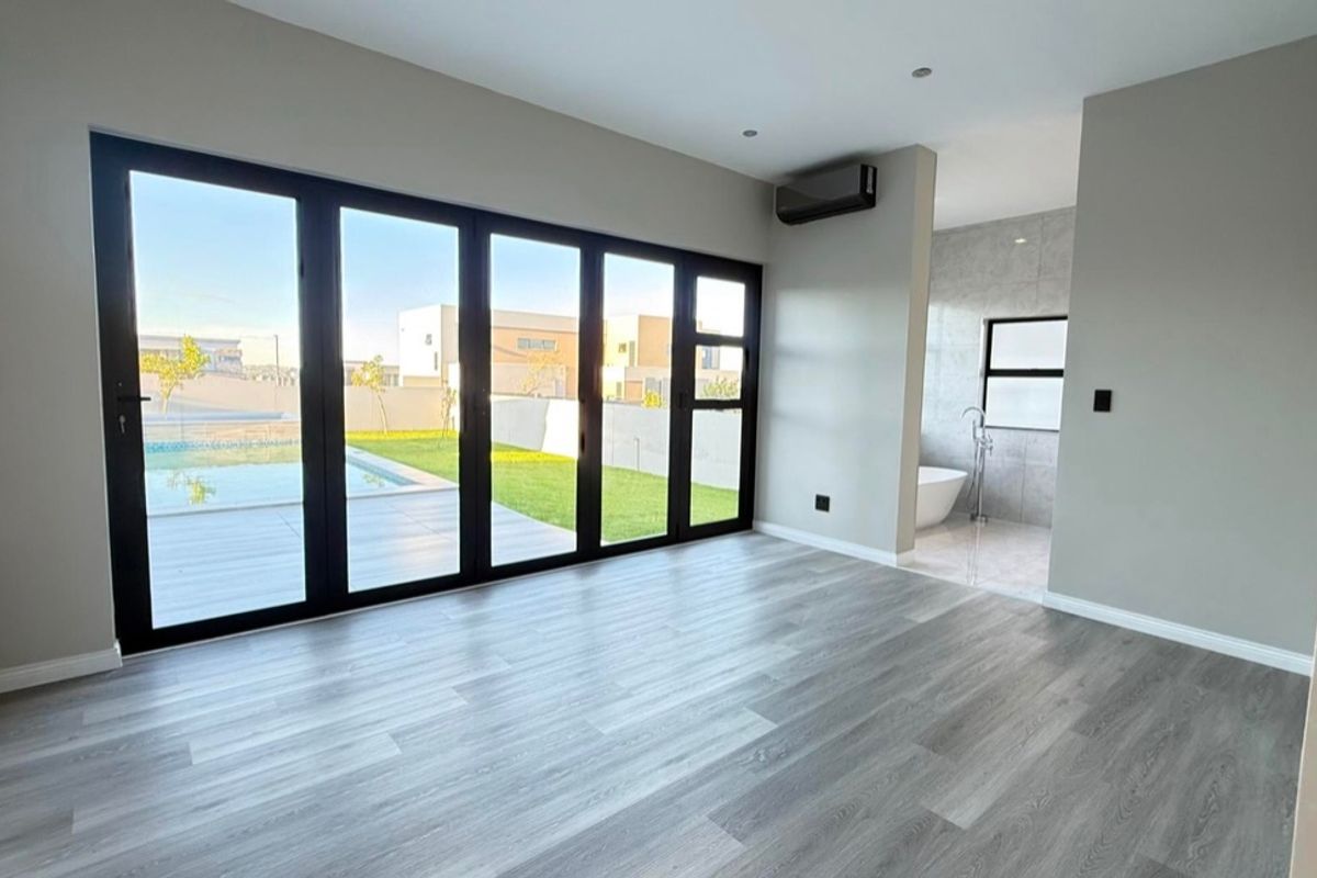 Spacious bedroom featuring modern laminate flooring, air conditioning, and large bi-fold doors opening to a pool area, with an integrated open-plan bathroom.