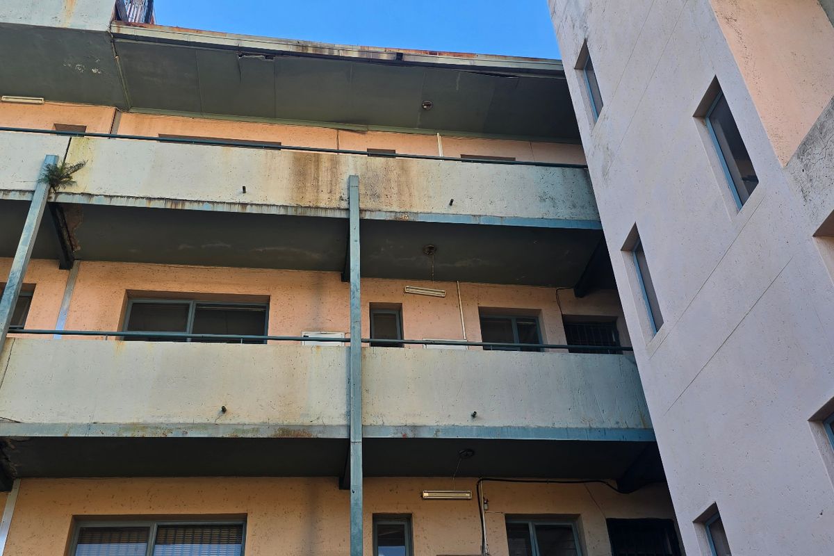 Exterior view of an apartment building showing multi-level balconies with visible signs of weathering, surface staining, and corrosion on the metal railings.
