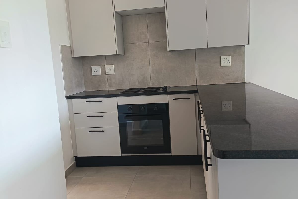 Modern kitchen featuring sleek built-in cabinetry, granite countertops, a built-in oven, gas hob, and neutral tiled flooring.