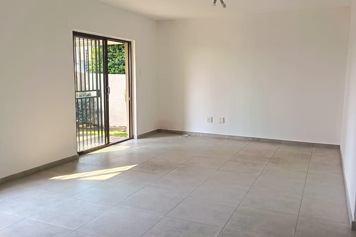 A spacious, empty living area featuring neutral tiled flooring and a sliding glass door with security gate providing access to the exterior.
