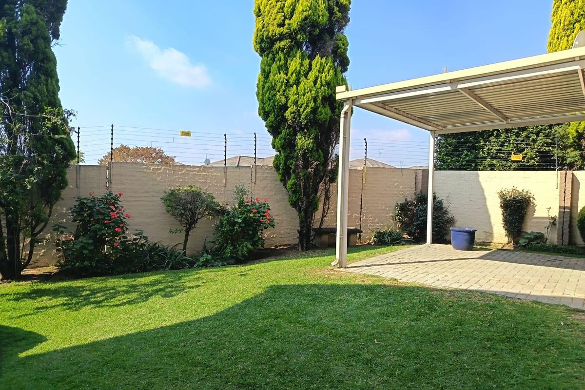 A private rear garden featuring a paved covered patio area, well-maintained lawn, and secure perimeter wall with electric fencing.