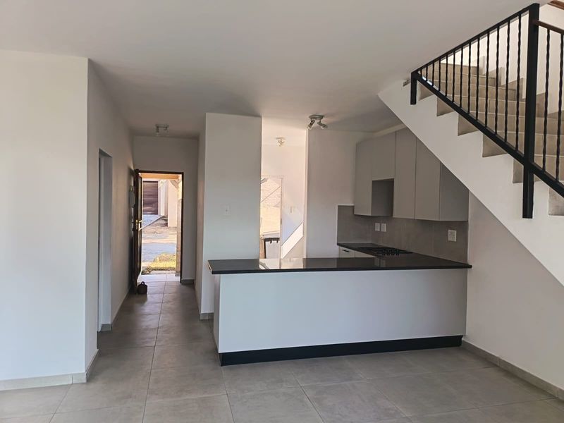 Open-plan living area featuring a modern kitchen with granite countertops, breakfast bar, and tiled flooring, adjacent to a staircase.
