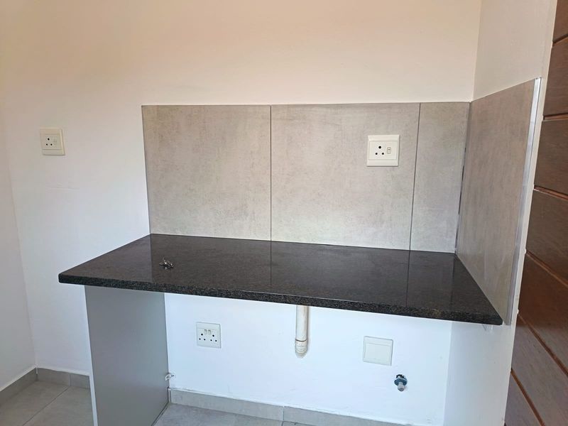 A clean, functional laundry or utility area featuring a dark granite countertop, tiled splashback, and dedicated plumbing and electrical connections for appliances.