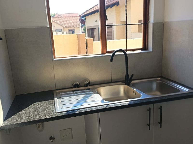 A compact kitchen area featuring a stainless steel double sink, modern black mixer tap, granite countertops, and tiled splashback with a window view.