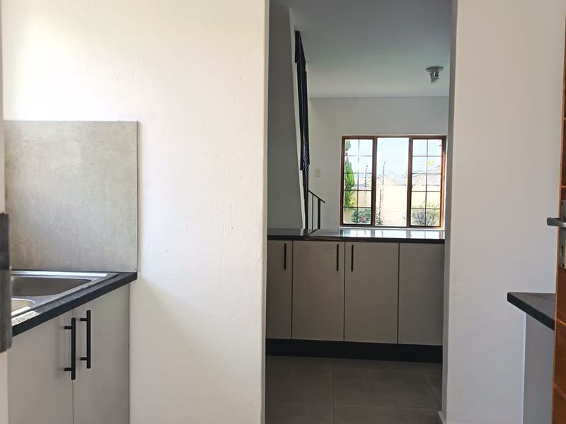 A clean, functional kitchen area featuring modern cabinetry, tiled flooring, and a view through to the adjacent living space.
