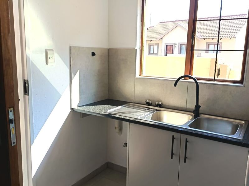 A compact scullery area featuring a stainless steel sink, granite countertops, built-in cabinetry, and tiled finishes, providing a functional prep or wash-up space.