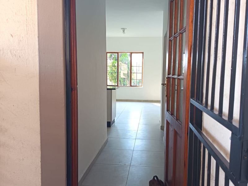 Entrance view into an open-plan living area featuring tiled flooring, a timber door, and a security gate.