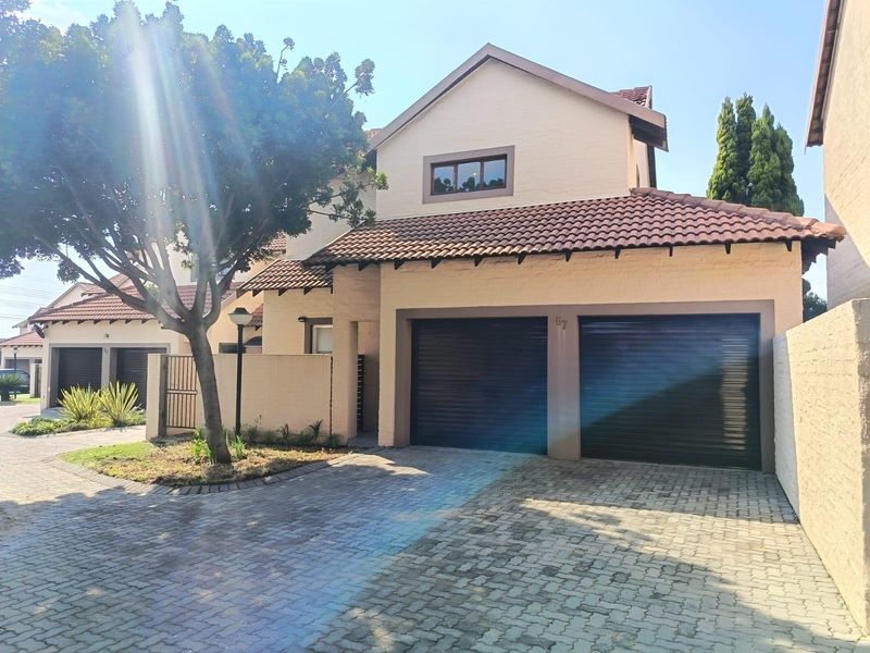 Front elevation of a townhouse featuring a double garage with roll-up doors, a paved driveway, and a tiled roof structure.