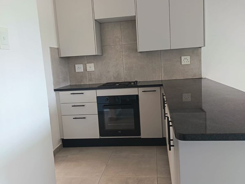 Modern kitchen featuring sleek built-in cabinetry, granite countertops, a built-in oven, gas hob, and neutral tiled flooring.