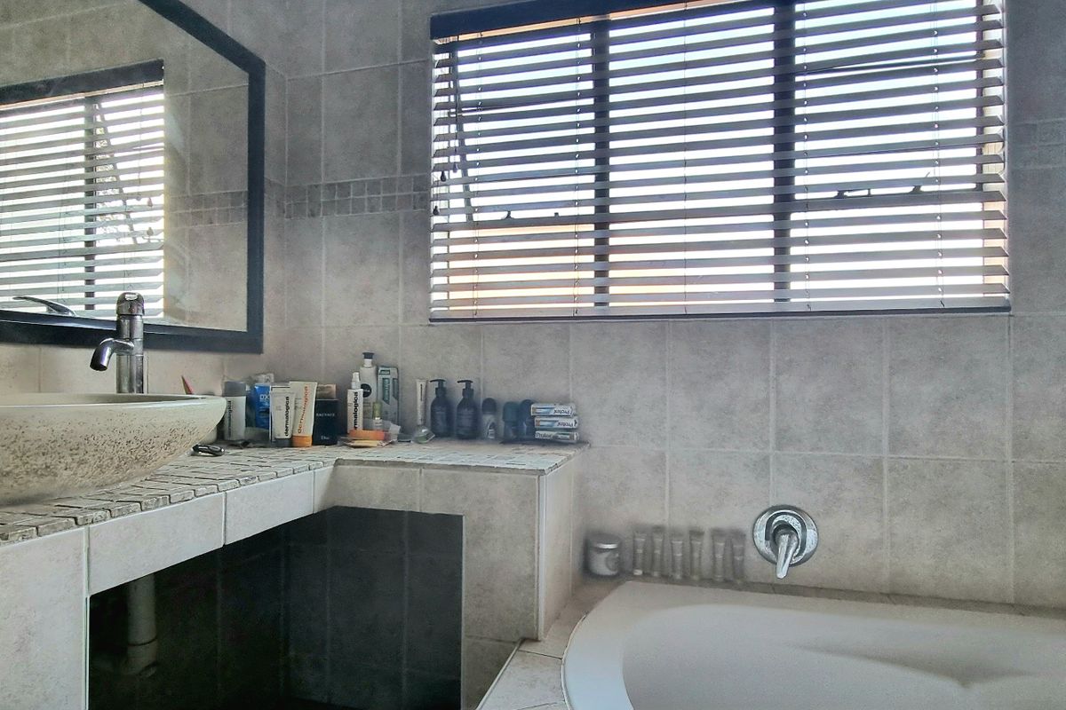 A functional bathroom featuring a tiled vanity with a vessel sink, a built-in bathtub, and neutral ceramic wall tiling.