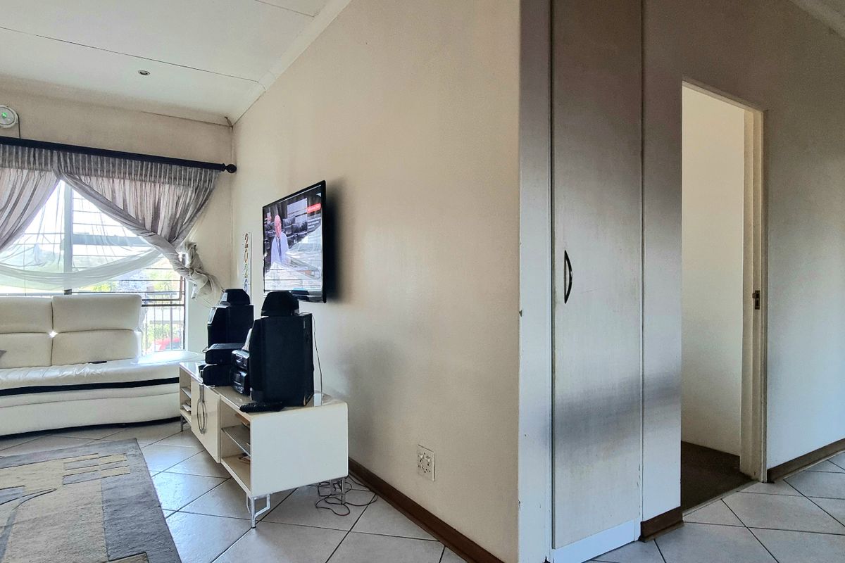 Open-plan living area featuring tiled flooring, recessed lighting, and a built-in storage cupboard, providing access to adjacent rooms.